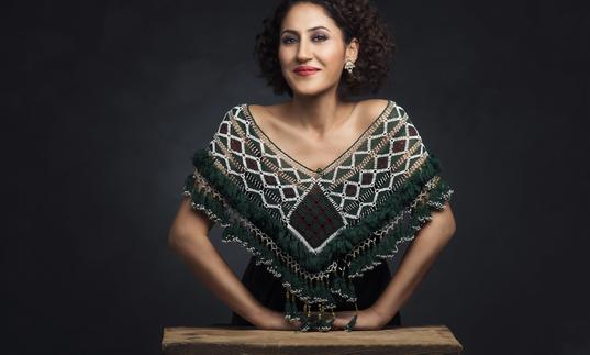 Aynur wearing an embroidered shawl leaning on a small wooden table