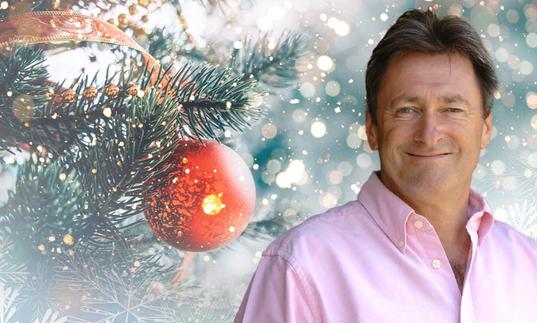 Alan Titchmarsh smiling, with a Christmas tree and bauble behind him