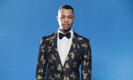 Davone Tines standing in front of a blue wall