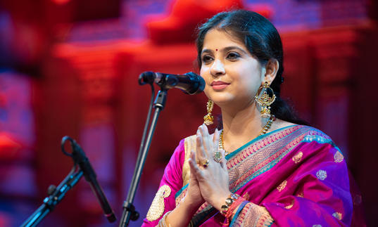 Kaushiki Chakraborty at a microphone, smiling with her hands palm together