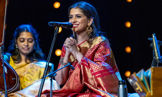 Kaushiki Chakraborty sitting at a microphone, smiling with her hands clasped together