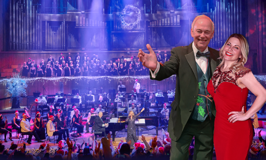 Jonathan Cohen and Louise Dearman smiling in front of an orchestra and choir