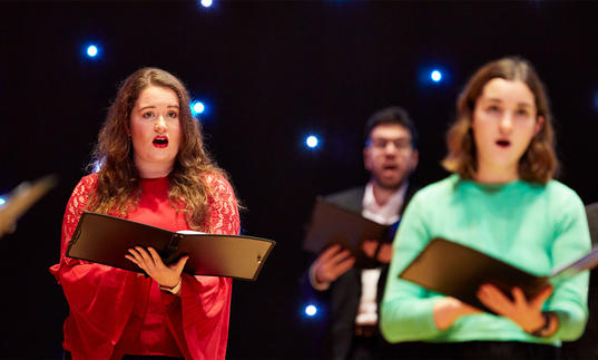 Singers with music in front of fairy lights in background