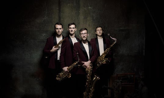 The Kebyart Ensemble stand holding their saxophones, looking at the camera