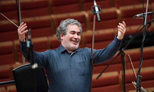Carlo Rizzi smiles with his arms up, conductor's baton in his right hand