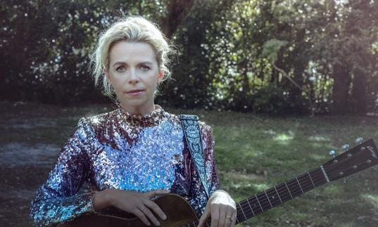 a photo of Aoife O'Donovan wearing a sequin top in a park with a guitar
