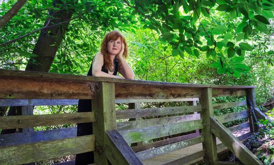 Sarah Cahill standing on a wooden bridge surrounded by trees