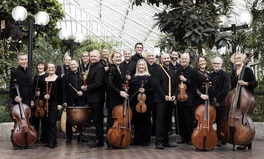 Players of the Academy of Ancient Music standing with their instruments in the Barbican Conservatory