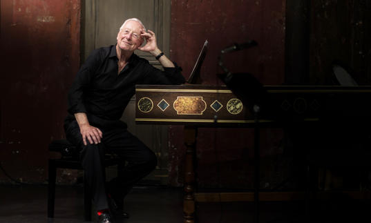 William Christie sitting at a harpsichord smiling