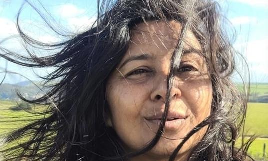 Davel Holvek Patel standing in a field, her hair is being blown by the wind