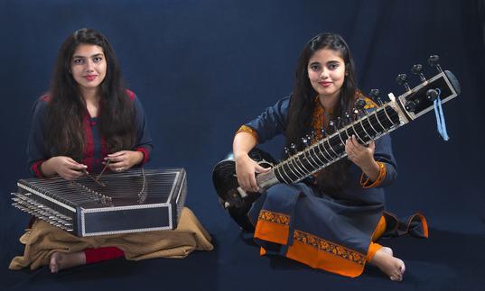 Sanskrati and Prakrati Wahane playing their instruments in front of a dark background