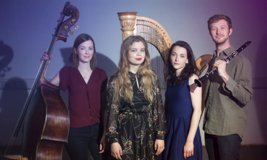 The Hermes Experiment standing with their instruments: a double bass, a clarinet and a harp