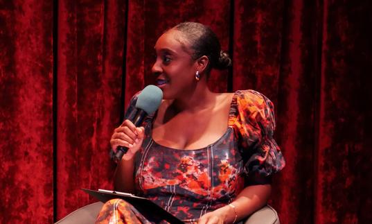 Black female in sitting in a chair holding a microphone