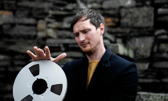 Erland Cooper, holding a film reel, wearing a suit 