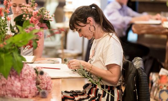 Woman drawing a vase of pink and green flowers