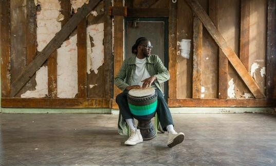 Yahael Camara Onono sitting on a chair looking away playing a drum rhythmically