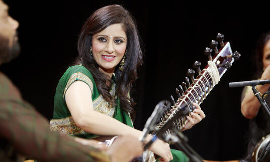 Roopa Panesar on stage playing an instrument smiling 