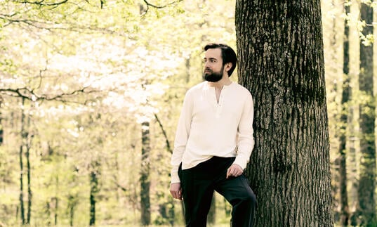 Daniil Trifonov standing next to a tree trunk