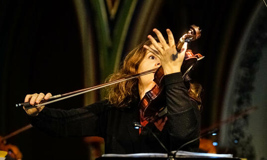 Patricia Kopatchinskaja plays her violin - it's held in front of the right hand side of her face 