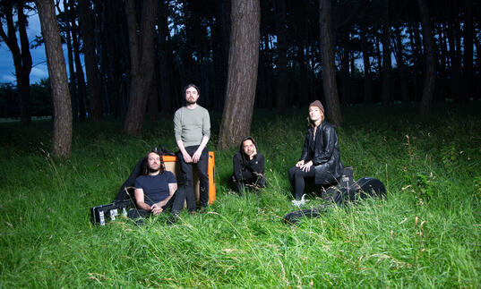 Group shot of Lankum sitting on a patch of moonlight grass next to a forest