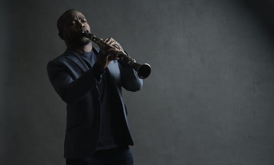 Anthony McGill playing his clarinet in front of a grey background