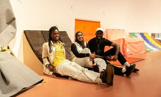 a photo of RESOLVE Collective sitting on their installation in The Curve gallery for them's the breaks