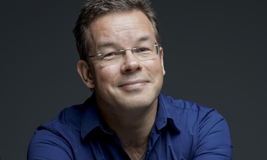 Antony Hermus smiling at camera wearing blue shirt and glasses