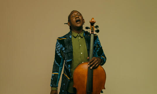 Abel Selaocoe looking upwards with his eyes closed, holding his cello