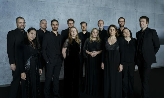 Members from Collegium Vocale Gent dressed in black, standing in front of a concrete wall