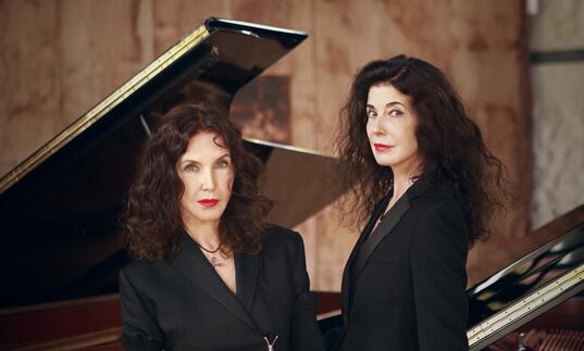 Katia and Marielle Labèque standing in front of two grand pianos