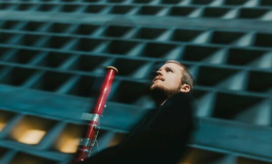 Mathis Stier holding his bassoon in front of a concrete building