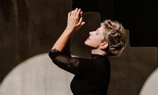 Side profile of Joyce DiDonato with her hands clasped and raised upwards