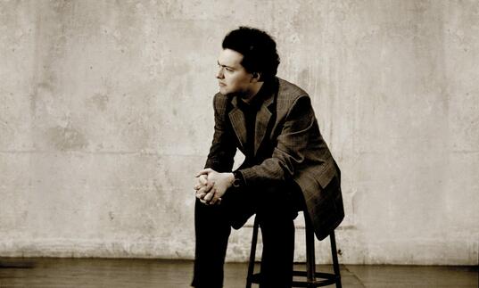 Evgeny Kissin sitting on a stool with his hands clasped
