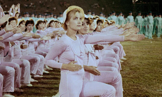 A group of cheerleaders in pink and white dresses do a choreographed dance.