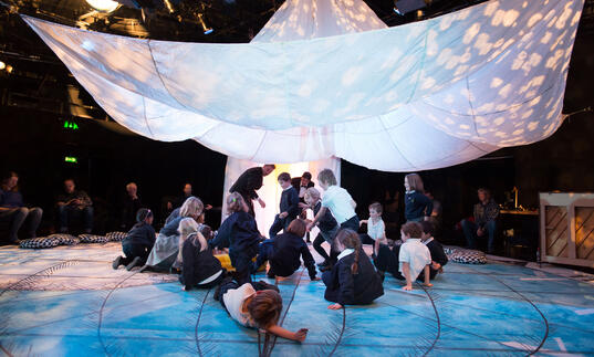 Children and their families gather underneath a large white parachute. 