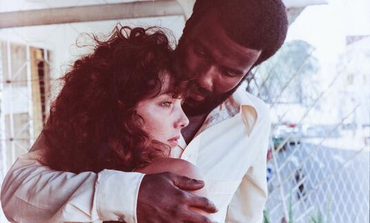 A man holds a woman whilst she looks out on a porch. 