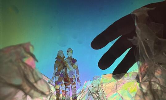 Two people crafted out of see through material stand before each other in a dream-like world. A hand reaches towards them.