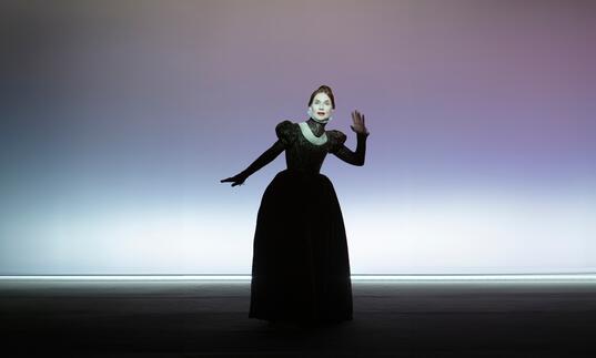 Actress Isabelle Huppert poses as Mary Stuart in an old-fashioned gown against a purple background. 