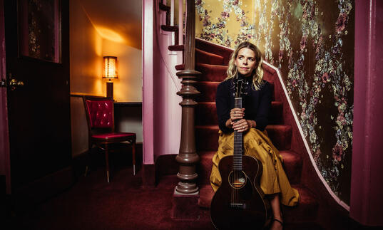 Aoife O'Donovan sits on purple staircase holding guitar