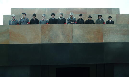 Stalin's peers stand on a concrete balcony dressed in military uniform