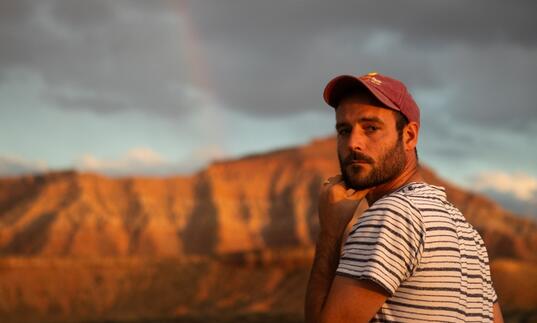 Roo Panes looks over his shoulder at the camera, surrounded by a rugged landscape