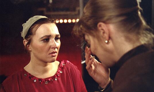 A woman looks on as another woman cries in front of her. 