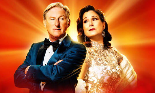 Actor Adrian Dunbar and musical star Stephanie J. Block stand side-by-side against a red and golden background.