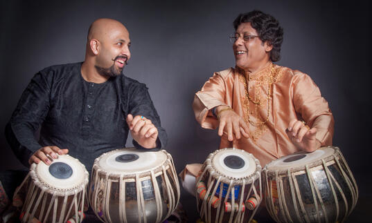 Anindo and Anubratta Chatterjee playing the tabla, smiling at each other