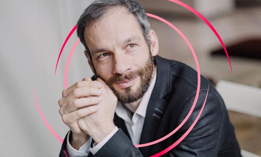 Dima Slobodeniouk clasping his hands in front of his face, with pink circular swirls around him