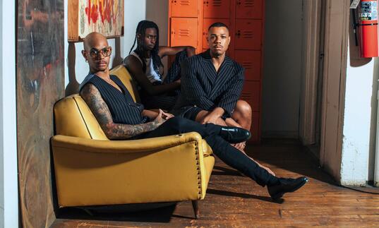 Davóne Tines, Khari Lucas and John Bitoy sitting on a yellow sofa