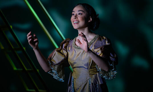 Guildhall School opera singer with arms raised, smiling against a green background