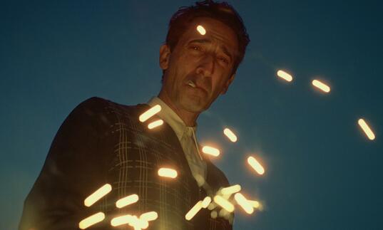 Adrien Brody stares down into camera, smoking
