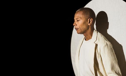 Jeff Mills under a spotlight wearing a white blazer and tshirt