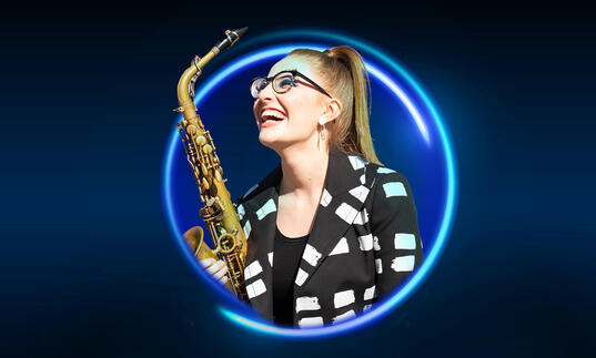 Jess Gillam holding a saxophone against a blue backdrop